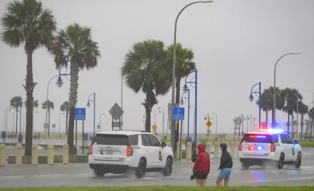 Cameron Henry, left, Owen Henry, and Stone Ridgeway, watch as Orleans Levee District Police patrol as rain and wind builds up from Hurricane Francine on Lakeshore Drive along Lake Ponchartrain in New Orleans, Wednesday, Sept. 11, 2024. (AP Photo/Matthew Hinton)