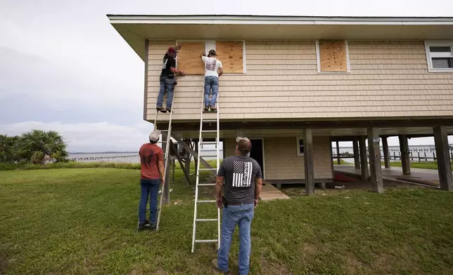 Jerry McCullen, top of ladder left, and Carson Baze, top of ladder right, put plywood over the windows of a house ahead of Hurricane Helene, expected to make landfall Thursday evening, in Alligator Point, Fla., Wednesday, Sept. 25, 2024. (AP Photo/Gerald Herbert)