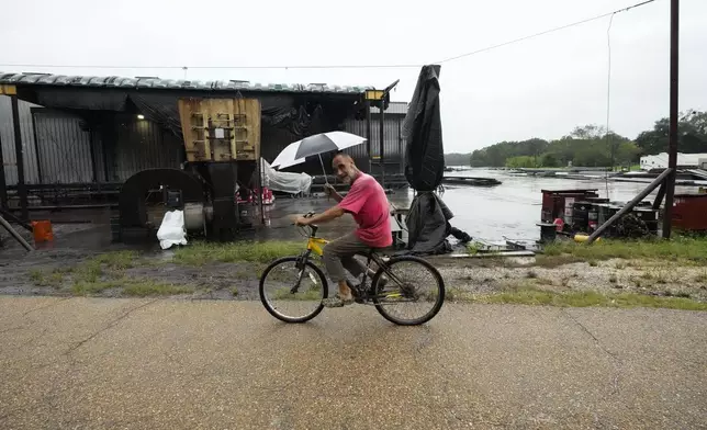 Kevin "Choupie" Badle, 67, rides his bike with an umbrella to buy more cigarettes at the store ahead of Hurricane Francine, expected to make landfall this evening, in Stephenville, La., Wednesday, Sept. 11, 2024. (AP Photo/Gerald Herbert)