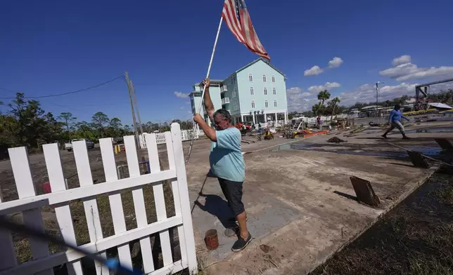 Daniel Dickert plants an American flag on his property were his boat shed was destroyed and his home damaged in the aftermath of Hurricane Helene, in Jena, Fla., Sunday, Sept. 29, 2024. (AP Photo/Gerald Herbert)