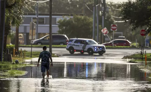 A man walks out of a street with water flooded from Hurricane Helene Friday, Sept. 27, 2024, in New Port Richey, Fla. (AP Photo/Mike Carlson)