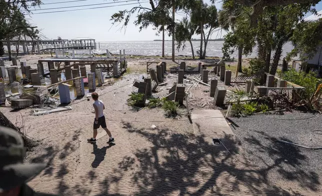 A person walks past building foundations along the water in the aftermath of Hurricane Helene, in Cedar Key, Fla., Friday, Sept. 27, 2024. (AP Photo/Gerald Herbert)