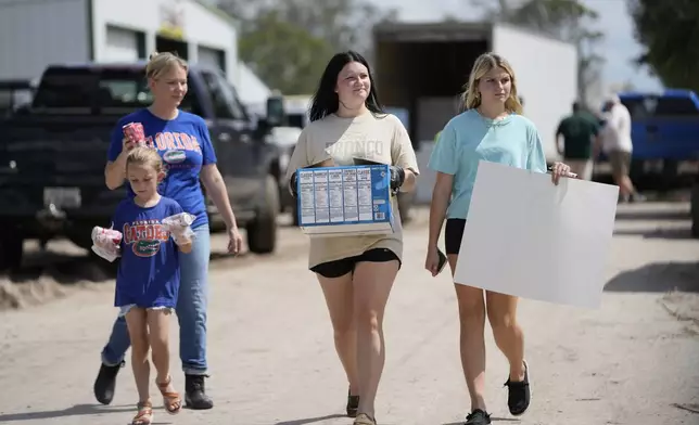 Volunteers Chelsea Marchant and her daughter Remi, along with Brennan Cordery, center, and Lynnlee Stratton, all of Dixie County, carry donations in the aftermath of Hurricane Helene, in Horseshoe Beach, Fla., Saturday, Sept. 28, 2024. (AP Photo/Gerald Herbert)