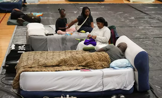 Sharonda and Victor Davis, of Tallahassee, sit with their children Victoria background left, and Amaya, background right, inside a hurricane evacuation shelter at Fairview Middle School, ahead of Hurricane Helene, expected to make landfall here today, in Leon County, Fla., Thursday, Sept. 26, 2024. (AP Photo/Gerald Herbert)