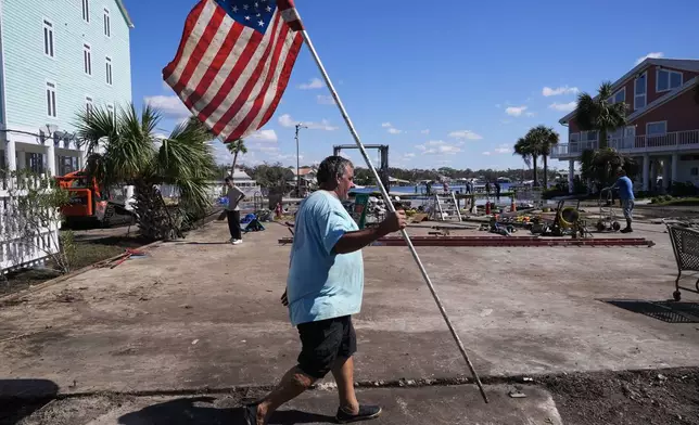 Daniel Dickert walks to plant an American flag on is property were his boat shed was destroyed and his home damaged in the aftermath of Hurricane Helene, in Jena, Fla., Sunday, Sept. 29, 2024. (AP Photo/Gerald Herbert)