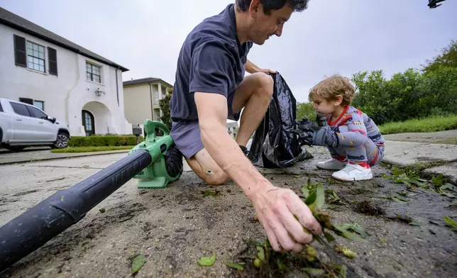 John Finney and his son Gabriel, 2, using gloves a little too big for him, clean up debris after Hurricane Francine near their home in Kenner, La., in Jefferson Parish, Thursday, Sept. 12, 2024. (AP Photo/Matthew Hinton)