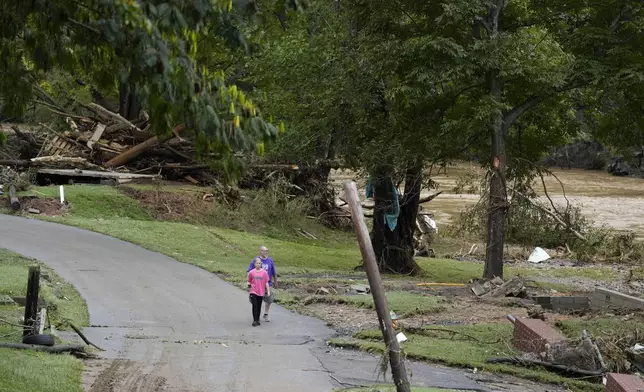 People walk along River St. near the Pigeon River where flood damage is seen Saturday, Sept. 28, 2024, in Newport, Tenn. (AP Photo/George Walker IV)