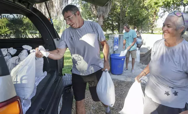 Karl Bohlmann, left, and Tangi Bohlmann, of Tarpon Springs, collect sandbags at a public site while residents prepare their homes for potential flooding, Tuesday, Sep 24, 2024, in Tarpon Springs, Fla., as the Tropical Storm Helene approaches. (Douglas R. Clifford/Tampa Bay Times via AP)