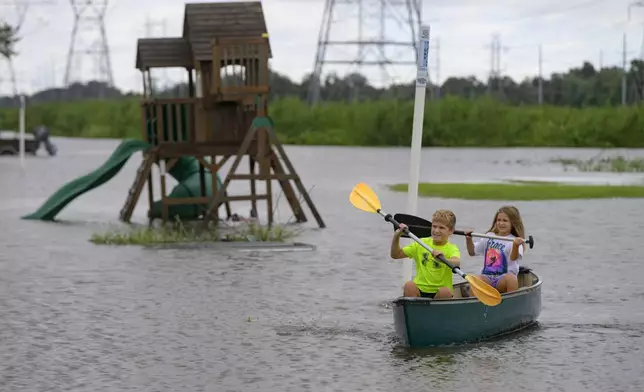 Siblings Avery, 10, and Grace LeBlanc, 7, canoe in their backyard next to playground equipment after flooding from Hurricane Francine in Montz, La., in St. Charles Parish, Thursday, Sept. 12, 2024. (AP Photo/Matthew Hinton)