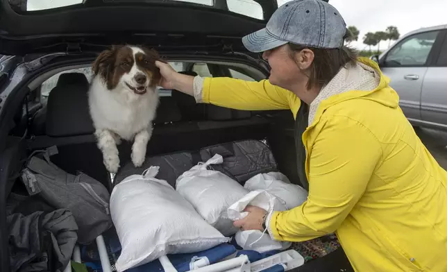 Lindsey Ranney and her dog Fig fill the trunk of Ranney's car with sandbags in preparation for Hurricane Francine from a pile of sand provided by Harrison County at the end of Courthouse Boulevard in Gulfport, Miss. on Tuesday, Sept. 10, 2024. (Hannah Ruhoff/The Sun Herald via AP)