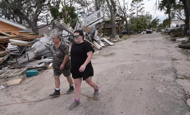 Charlene Huggins, and her daughter-in-law, Katelyn Huggins, right, walk past the destruction on their street in the aftermath of Hurricane Helene, in Horseshoe Beach, Fla., Saturday, Sept. 28, 2024. (AP Photo/Gerald Herbert)