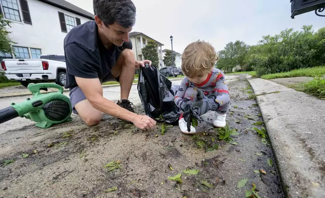 John Finney and his son Gabriel, 2, using gloves, clean up debris after Hurricane Francine near their home in Kenner, La., in Jefferson Parish, Thursday, Sept. 12, 2024. (AP Photo/Matthew Hinton)