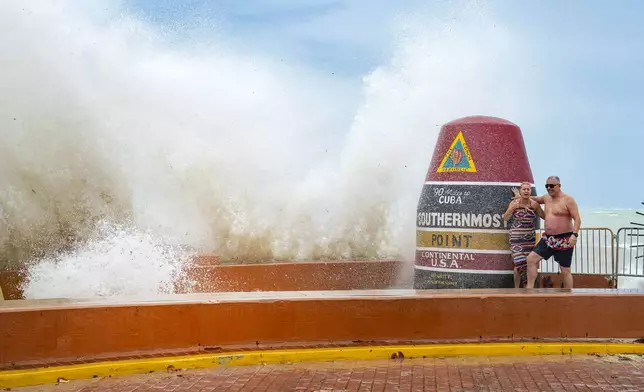 Visitors to the Southernmost Point marker in Key West, Fla., are hit by wind driven waves from approaching Hurricane Helene on Wednesday, Sept. 25, 2024. (Rob O'Neal/The Key West Citizen via AP)