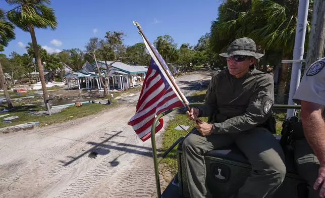 Officer Nate Martir, a law enforcement officer from the Florida Fish Wildlife and Conservation Commission, holds an American flag that was lying on the ground amid debris, while patrolling from a high water capable swamp buggy, in the aftermath of Hurricane Helene, in Cedar Key, Fla., Friday, Sept. 27, 2024. (AP Photo/Gerald Herbert)