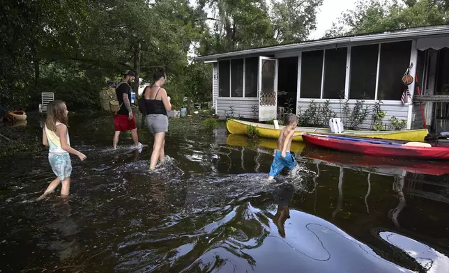 Dustin Holmes, rear, his girlfriend Hailey Morgan, and her children Aria Skye Hall, 7, left, and Kyle Ross, 4, right, arrive to their flooded home in the aftermath of Hurricane Helene, Friday, Sept. 27, 2024, in Crystal River, Fla. (AP Photo/Phelan M. Ebenhack)