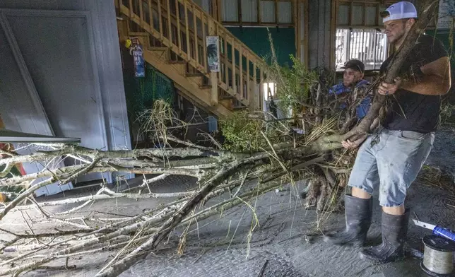 Jansen Pellegrin, back right, and Drew Foret, right, remove a small tree that floated into a living room area at their fishing camp from Hurricane Francine in Terrebonne Parish, La., Thursday, Sept. 12, 2024. (Chris Granger/The Times-Picayune/The New Orleans Advocate via AP)