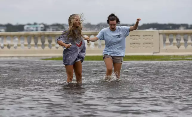 Camryn Frick, left, and Jillian Sternick, both 22, and of Tampa, hold hands as they cross a flooded street together along Bayshore Boulevard on Thursday, Sept. 26, 2024, in Tampa, Fla. (Jefferee Woo/Tampa Bay Times via AP)