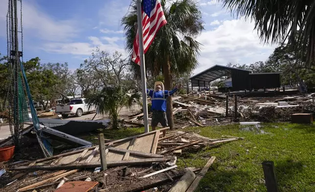 Chris Jordan, maintenance manager for Horseshoe Beach, hoists an American flag over the ruins of the city hall, in the aftermath of Hurricane Helene, in Horseshoe Beach, Fla., Saturday, Sept. 28, 2024. (AP Photo/Gerald Herbert)