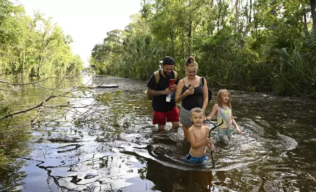 Dustin Holmes, rear left, his girlfriend Hailey Morgan, and her children Aria Skye Hall, 7, right, and Kyle Ross, 4, walk through a flooded road while returning to their home after Hurricane Helene passed near the area, Friday, Sept. 27, 2024, in Crystal River, Fla. (AP Photo/Phelan M. Ebenhack)