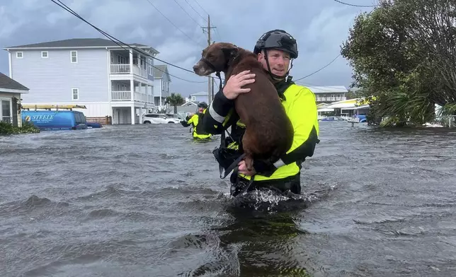 In this image provided by the Wilmington, N.C., Fire Department, a firefighter carries a dog through floodwaters, Monday, Sept. 16, 2024, in Kure Beach, N.C., (Wilmington Fire Department via AP)