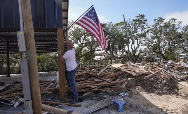 John Taylor puts up an American flag on his destroyed property in the aftermath of Hurricane Helene, in Horseshoe Beach, Fla., Saturday, Sept. 28, 2024. (AP Photo/Gerald Herbert)