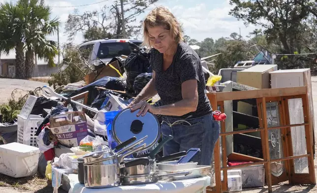 Susan Merritt, of Knoxville, Tenn., tries to clean and salvage pots and pans from her aunt's destroyed home in the aftermath of Hurricane Helene, in Steinhatchee, Fla., Sunday, Sept. 29, 2024. (AP Photo/Gerald Herbert)