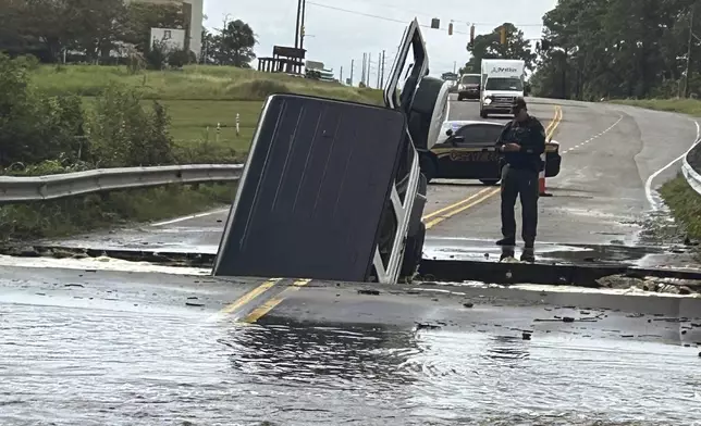 This photo provided by Brunswick County Sheriff's Office shows a police officer checking on a vehicle that fell into a sinkhole on a highway in Brunswick County, N.C., after a storm dropped historic amounts of rain, Monday, Sept. 16, 2024. (Brunswick County Sheriff's Office via AP)