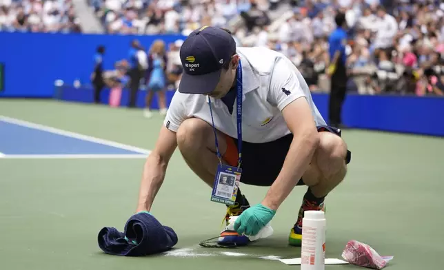 Court attendant Ethan Davison cleans up an area on the court where Jack Draper, of Great Britain, vomited in the second set against Jannik Sinner, of Italy, during the men's singles semifinal of the U.S. Open tennis championships, Friday, Sept. 6, 2024, in New York. (AP Photo/Frank Franklin II)