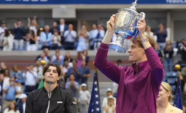 Jannik Sinner, of Italy, holds the championship trophy as Taylor Fritz, of the United States, looks on after sinner won the men's singles final of the U.S. Open tennis championships, Sunday, Sept. 8, 2024, in New York. (AP Photo/Kirsty Wigglesworth)