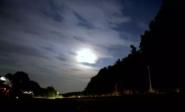 The moon shines over people parked at a scenic overlook to watch for aurora borealis in Alton Bay, New Hampshire as Canada and northern U.S. cities experience moderate solar storms, Thursday, Sept. 12, 2024. (AP Photo/Caleb Jones)