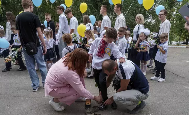 Parents help their son before the traditional ceremony for the first day of school in Zaporizhzhia, Ukraine, Sunday Sept. 1, 2024. Zaporizhzhia schoolchildren celebrated the traditional first day of school near the frontline. With the front just 40 kilometers away, the war is never far from the minds of teachers and families. (AP Photo/Evgeniy Maloletka)