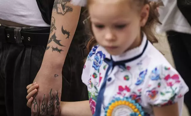 A first-grade girl holds the hand of her older schoolmate and walks to the traditional ceremony for the first day of school in Zaporizhzhia, Ukraine, Sunday Sept. 1, 2024. Zaporizhzhia schoolchildren celebrated the traditional first day of school near the frontline. With the front just 40 kilometers away, the war is never far from the minds of teachers and families. (AP Photo/Evgeniy Maloletka)