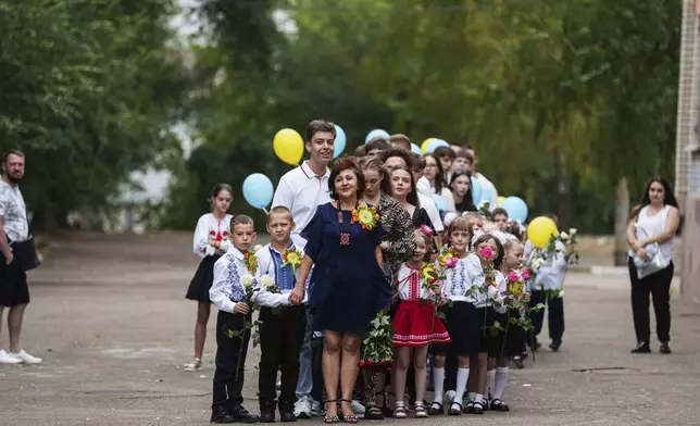 First-grades wait with a teacher for the start of the traditional ceremony for the first day of school in Zaporizhzhia, Ukraine, Sunday Sept. 1, 2024. Zaporizhzhia schoolchildren celebrated the traditional first day of school near the frontline. With the front just 40 kilometers away, the war is never far from the minds of teachers and families. (AP Photo/Evgeniy Maloletka)