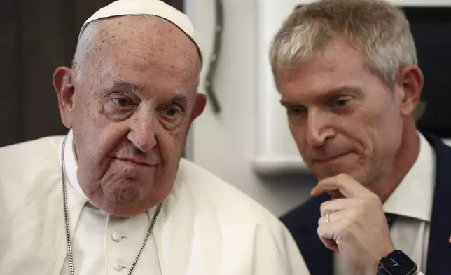 Pope Francis listens to Vatican spokesman Matteo Bruni aboard the papal plane on his flight back after his 12-day journey across Southeast Asia and Oceania, Friday, Sept. 13, 2024. (Guglielmo Mangiapane/Pool Photo via AP)