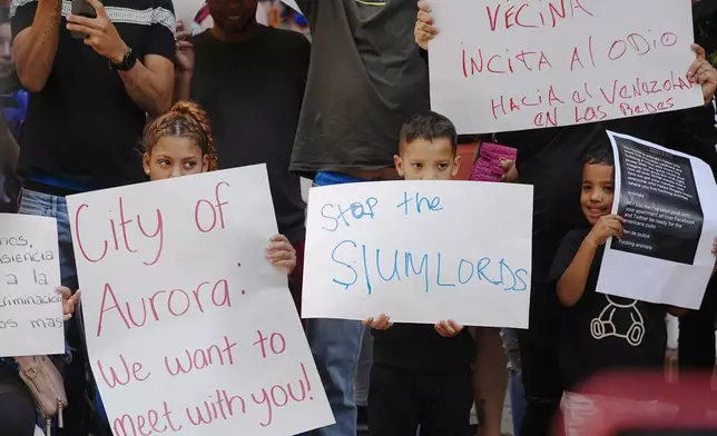 Residents hold up placards during a rally staged by the East Colfax Community Collective to address chronic problems in the apartment buildings occupied by people displaced from their home countries in central and South America Tuesday, Sept. 3, 2024, in Aurora, Colo. (AP Photo/David Zalubowski)