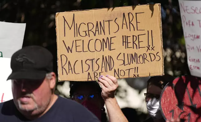 A protester holds up a placard during a rally staged by the East Colfax Community Collective to address chronic problems in the apartment buildings occupied by people displaced from their home countries in central and South America Tuesday, Sept. 3, 2024, in Aurora, Colo. (AP Photo/David Zalubowski)