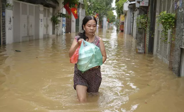 Local resident Nguyen Thi Hoa carries food to her home in a flooded street in the aftermath of Typhoon Yagi, in Hanoi, Vietnam on Thursday, Sept. 12, 2024. (AP Photo/Hau Dinh)