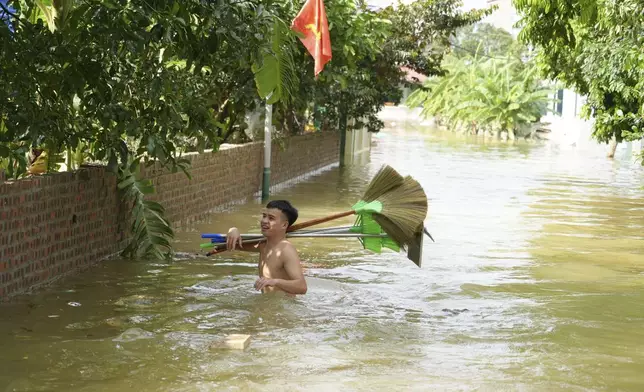 A man wades in flood carrying brooms to clean up houses as flood starts to recede in the aftermath of Typhoon Yagi in An Lac village, Hanoi, Vietnam Friday, Sept. 13, 2024. (AP Photo/Hau Dinh)