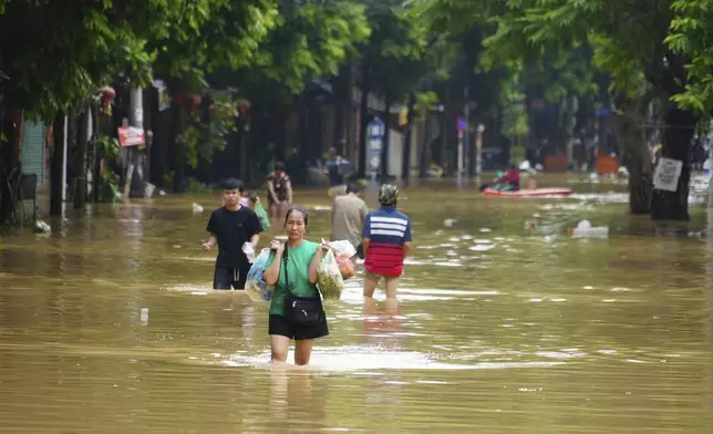 A woman carrying food wades in a flooded street in the aftermath of Typhoon Yagi, in Hanoi, Vietnam on Thursday, Sept. 12, 2024. (AP Photo/Hau Dinh)