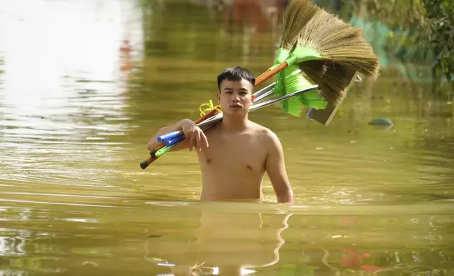 A man wades in flood carrying brooms to clean up houses as flood starts to recede in the aftermath of Typhoon Yagi in An Lac village, Hanoi, Vietnam Friday, Sept. 13, 2024. (AP Photo/Hau Dinh)