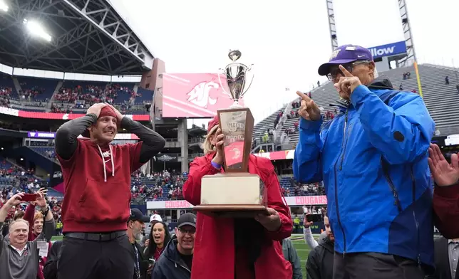 Washington State head coach Jake Dickert looks over at the Apple Cup trophy as Governor Jay Inslee, right, and wife Trudi Inslee, center, present him with the trophy to celebrate a 24-19 win over Washington after an NCAA college football game Saturday, Sept. 14, 2024, in Seattle. (AP Photo/Lindsey Wasson)