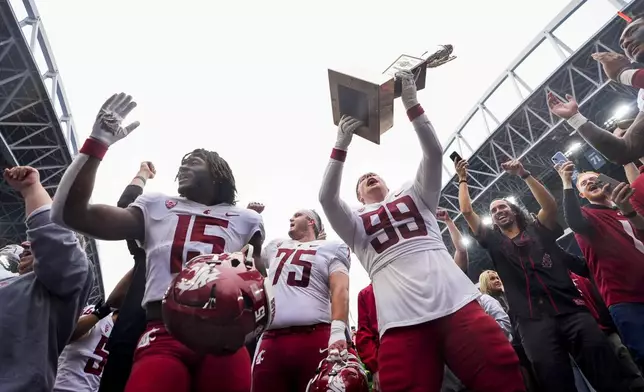 Washington State defensive tackle Bryson Lamb (99) holds up the Apple Cup Trophy while celebrating with offensive lineman Noah Dunham (75) and running back Djouvensky Schlenbaker (15) after beating Washington 24-19 in an NCAA college football game Saturday, Sept. 14, 2024, in Seattle. (AP Photo/Lindsey Wasson)