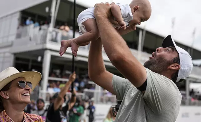 Scottie Scheffler holds his son Bennett Ezra Scheffler as his wife Meredith Scudder looks on the 18th green after Scheffler won the final round of the Tour Championship golf tournament, Sunday, Sept. 1, 2024, in Atlanta. (AP Photo/Mike Stewart)