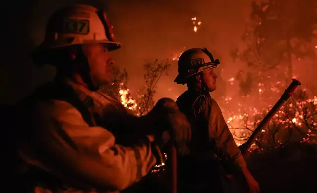 Firefighters are illuminated by the glow of the Bridge Fire in Wrightwood, Calif., Tuesday, Sept. 10, 2024. (AP Photo/Jae C. Hong)