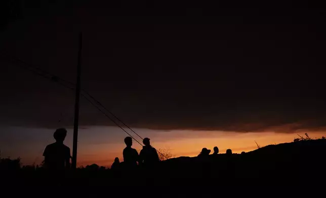 People watch from a hilltop under a layer of smoke from the Airport Fire as the sun sets, Monday, Sept. 9, 2024, in Trabuco Canyon, Calif. (AP Photo/Gregory Bull)