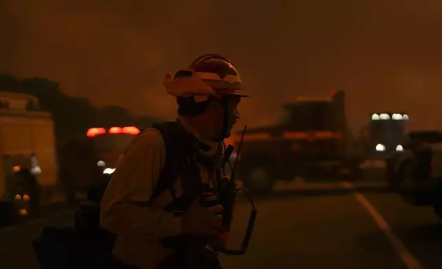 A firefighter crosses a road as the Airport Fire advances Tuesday, Sept. 10, 2024, in El Cariso, an unincorporated community in Riverside County, Calif. (AP Photo/Eric Thayer)