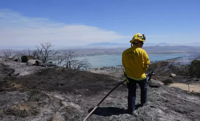 A Riverside County Fire Dept. firefighter monitors for hot spots overlooking Lake Elsinore after the Airport Fire swept through Wednesday, Sept. 11, 2024, in El Cariso Village, in unincorporated Riverside, County, Calif. (AP Photo/Gregory Bull)