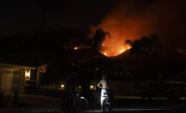 People watch flames from the Airport Fire as it envelops a hill behind homes Monday, Sept. 9, 2024, in Trabuco Canyon, Calif. (AP Photo/Gregory Bull)