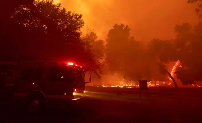 A fire engine is driven past a fire-engulfed structure as crews battle the Airport Fire Tuesday, Sept. 10, 2024, in El Cariso, an unincorporated community in Riverside County, Calif. (AP Photo/Etienne Laurent)