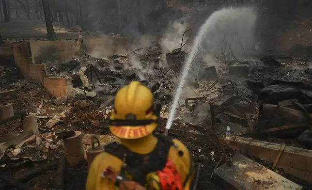 A firefighter hoses down hot spots on a fire-ravaged property while battling the Bridge Fire Wednesday, Sept. 11, 2024, in Wrightwood, Calif. (AP Photo/Eric Thayer)